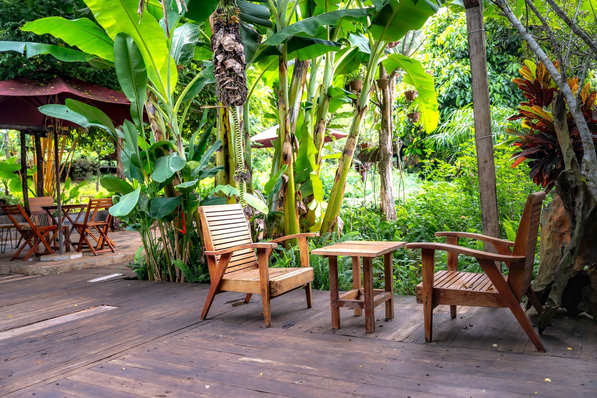 Wooden chairs and table in a lush tropical garden setting.